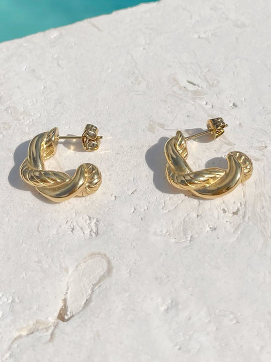 A pair of gold huggie hoop earrings with a twisted, braided design, inspired by Greek goddesses.