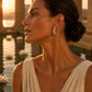 A delicate silver hoop earring, set against a warm, golden sunset background with classical columns and water lilies.
