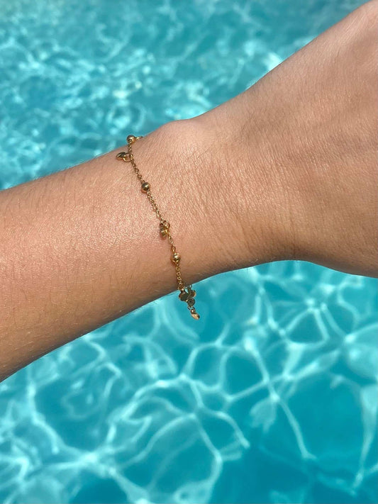 A delicate gold chain bracelet with small bead details and a tiny dangling charm, waterproof jewellery.
