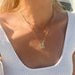 A woman wearing a delicate gold evil eye necklace with a square pendant featuring a blue zircon aquamarine gemstone and white zirconia gemstones, layered over a thin gold chain. Protection Jewelry.