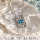 Silver Evil Eye Necklace with a blue evil eye stone on a textured sunburst pendant, styled on a glass shell in sunlit water.
