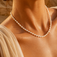 A delicate strand of white freshwater pearls, styled with a light beige draped top under warm golden sunlight.