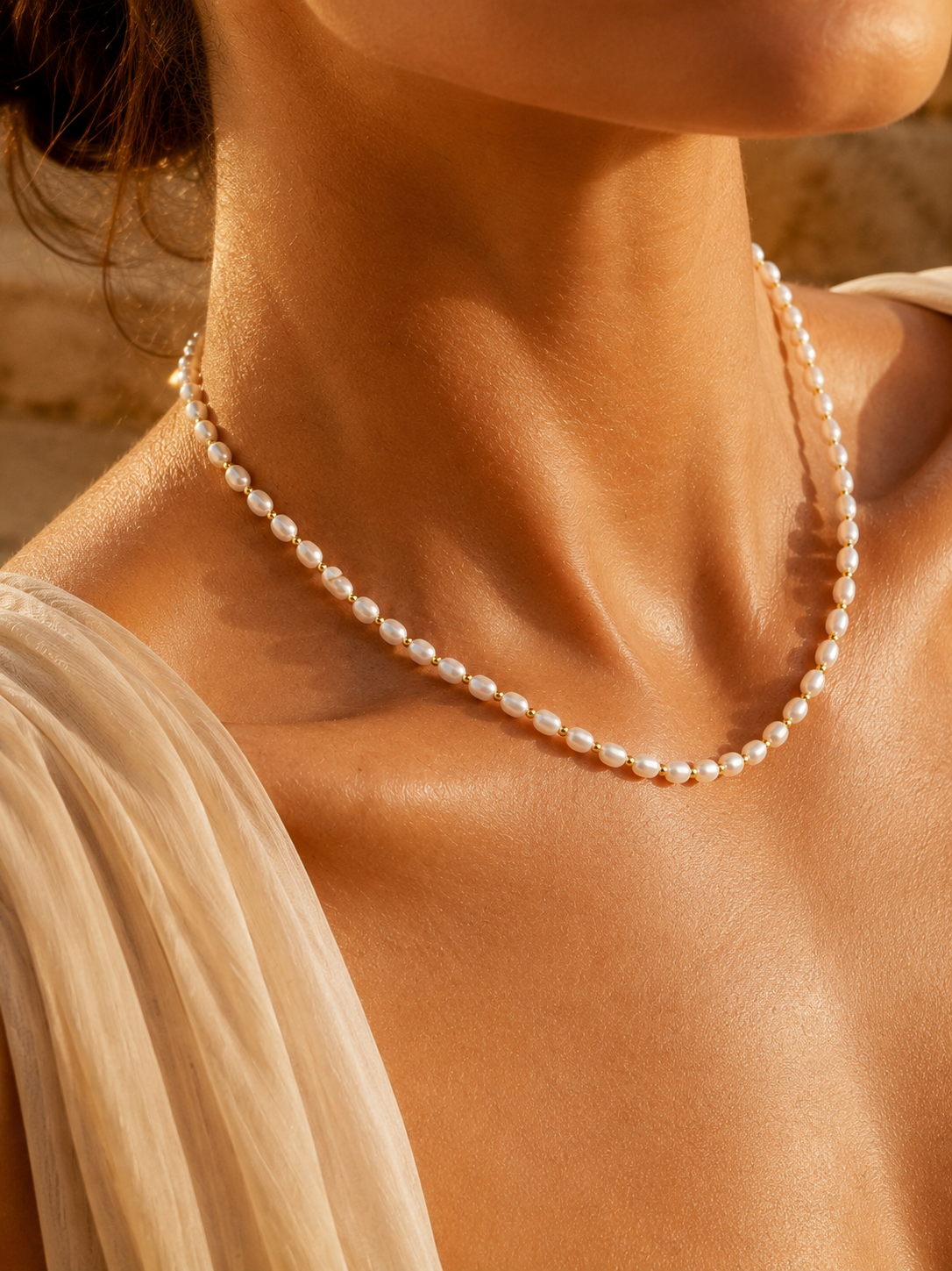 A delicate strand of white freshwater pearls, styled with a light beige draped top under warm golden sunlight.