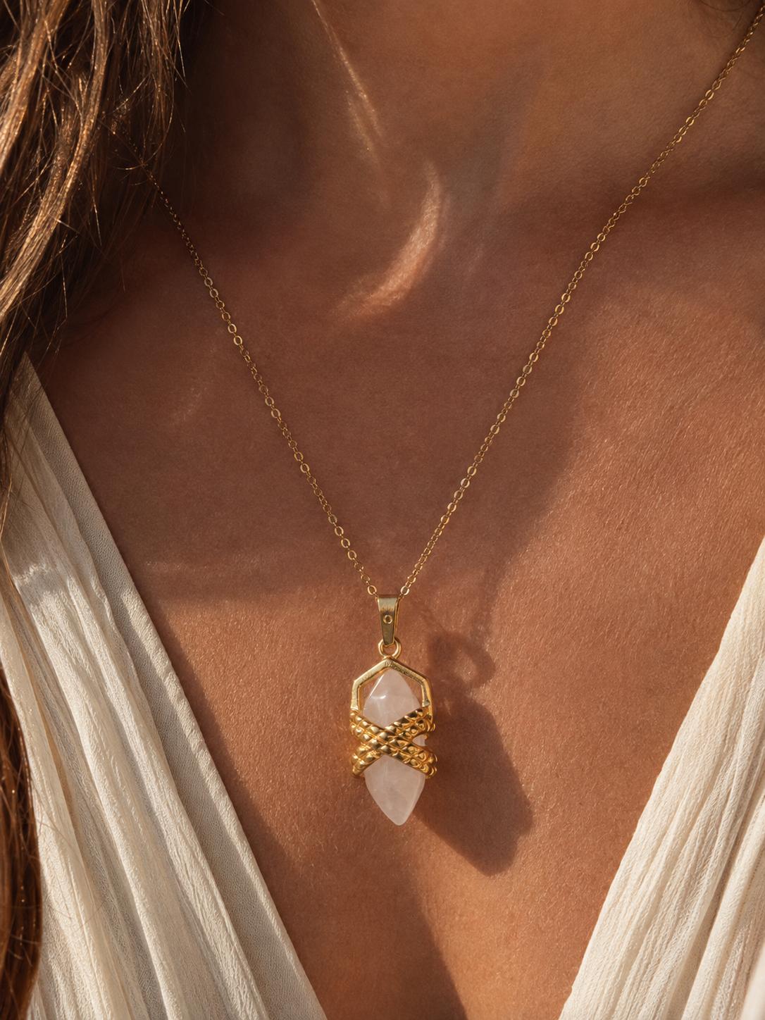 Close-up of a woman wearing a gold quartz crystal pendant necklace on a fine chain in warm natural sunlight.