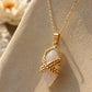 Close-up of a gold quartz crystal pendant necklace on a fine chain displayed on textured sandstone in warm natural light.