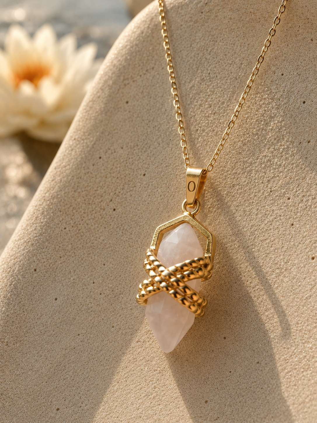 Close-up of a gold quartz crystal pendant necklace on a fine chain displayed on textured sandstone in warm natural light.