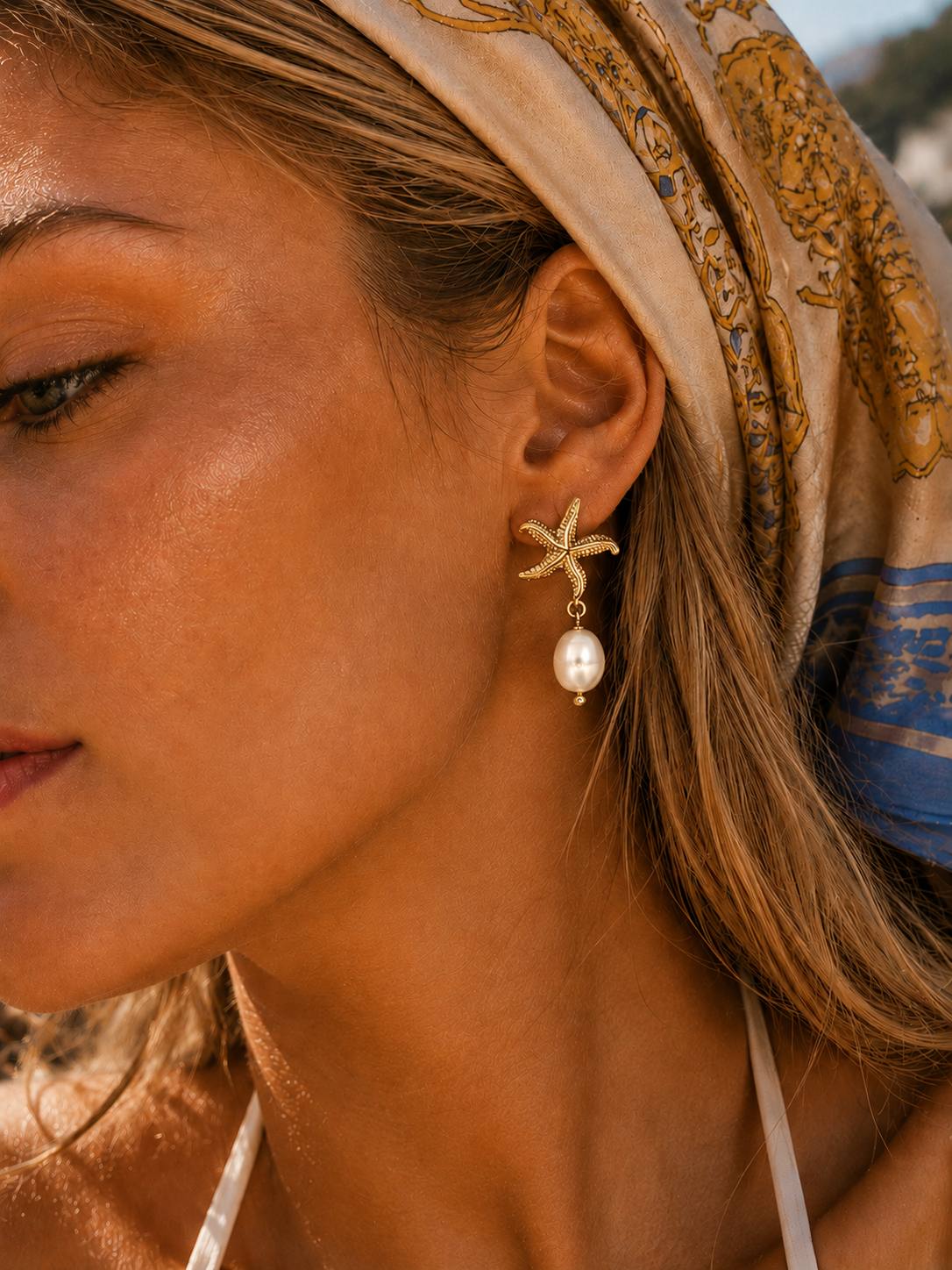 Close-up of the Maris gold starfish earrings featuring textured starfish detailing and a pearl drop