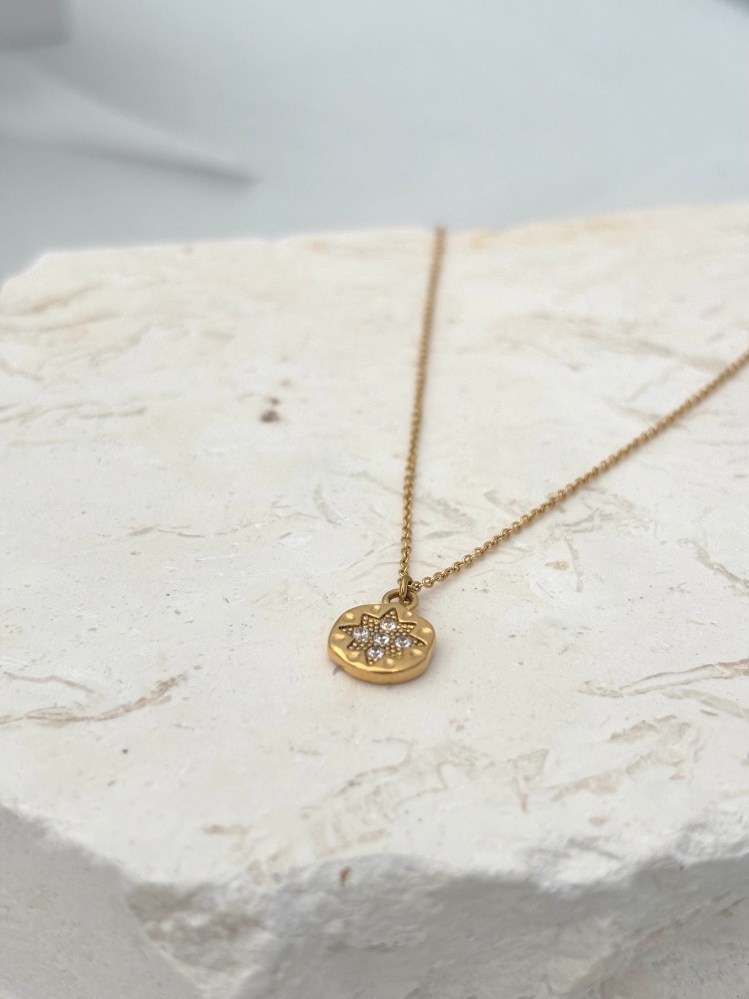 A delicate gold chain necklace with a small round pendant featuring a floral star design set with tiny clear stones, waterproof jewellery 