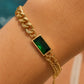 A gold chain bracelet with a rectangular green emerald-cut stone, worn on a person's wrist.