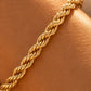 A close-up of a gold rope-style chain bracelet worn on a warm tan wrist or display form.