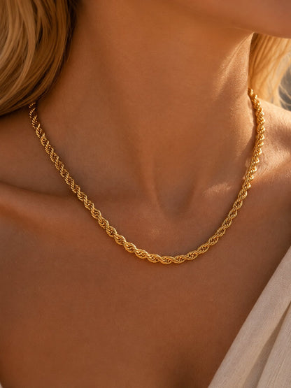 A close-up of a woman's neck and upper chest wearing a gold chain necklace with a twisted rope or braided link design.