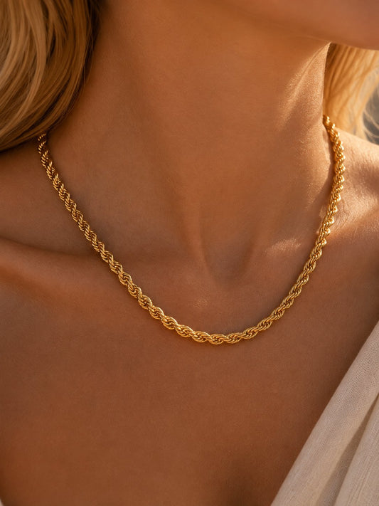 A close-up of a woman's neck and upper chest wearing a gold chain necklace with a twisted rope or braided link design.