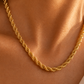 A close-up of a gold rope chain necklace worn on a model's neck, showing the detailed twisted links of the chain against warm skin tones.