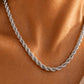 A close-up of a silver twisted rope chain necklace worn on a model's neck, showing the detailed links against warm skin tones.