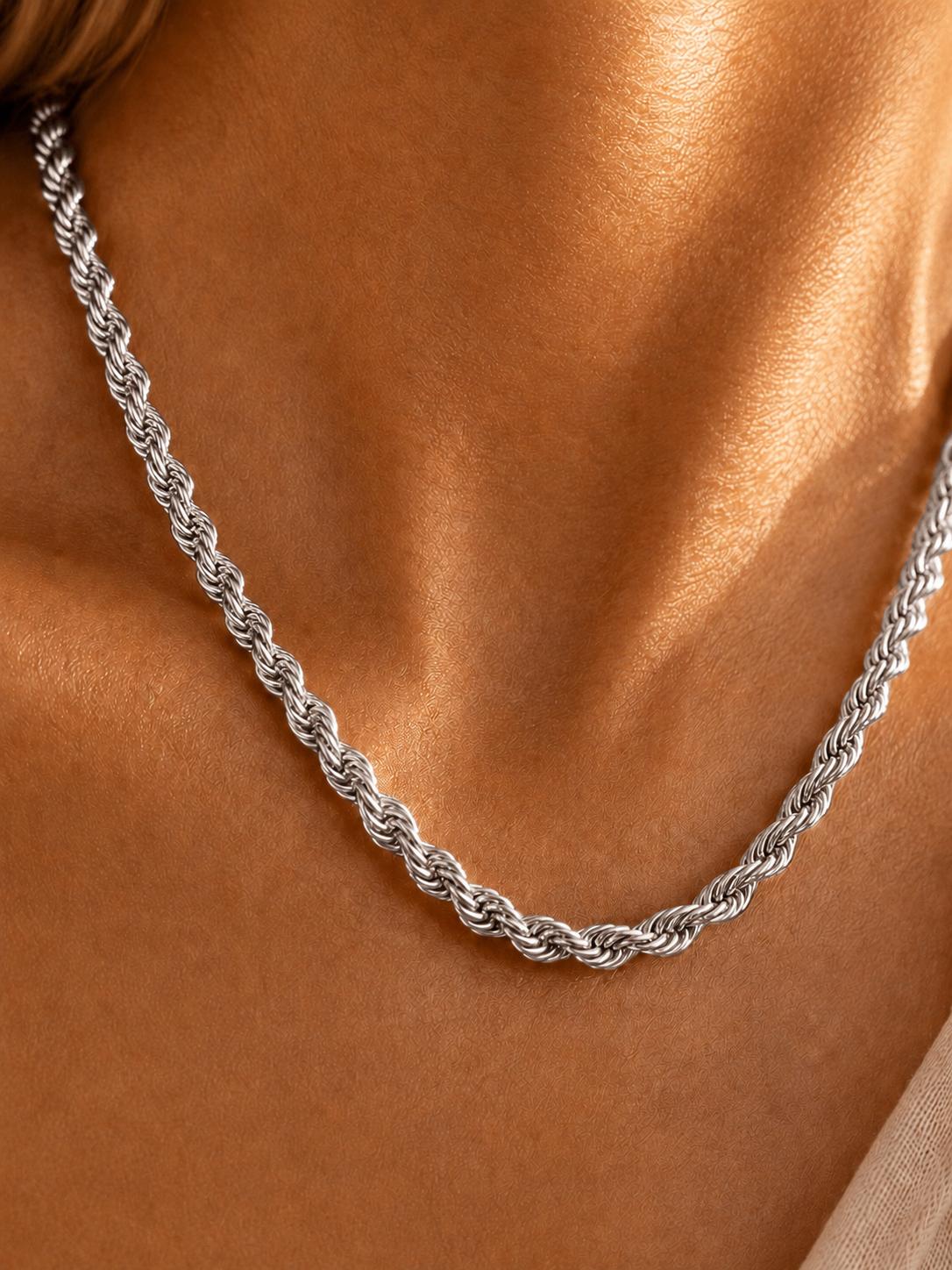 A close-up of a silver twisted rope chain necklace worn on a model's neck, showing the detailed links against warm skin tones.
