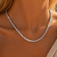 A close-up of a silver twisted rope chain necklace worn on a model's neck, with warm golden sunlight highlighting the metallic texture.
