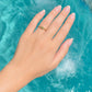 A gold ring with a small green stone set on a person's ring finger, shown against a bright turquoise swimming pool background.