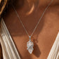 Close-up of a woman wearing a silver quartz crystal pendant necklace on a fine chain in warm natural sunlight.
