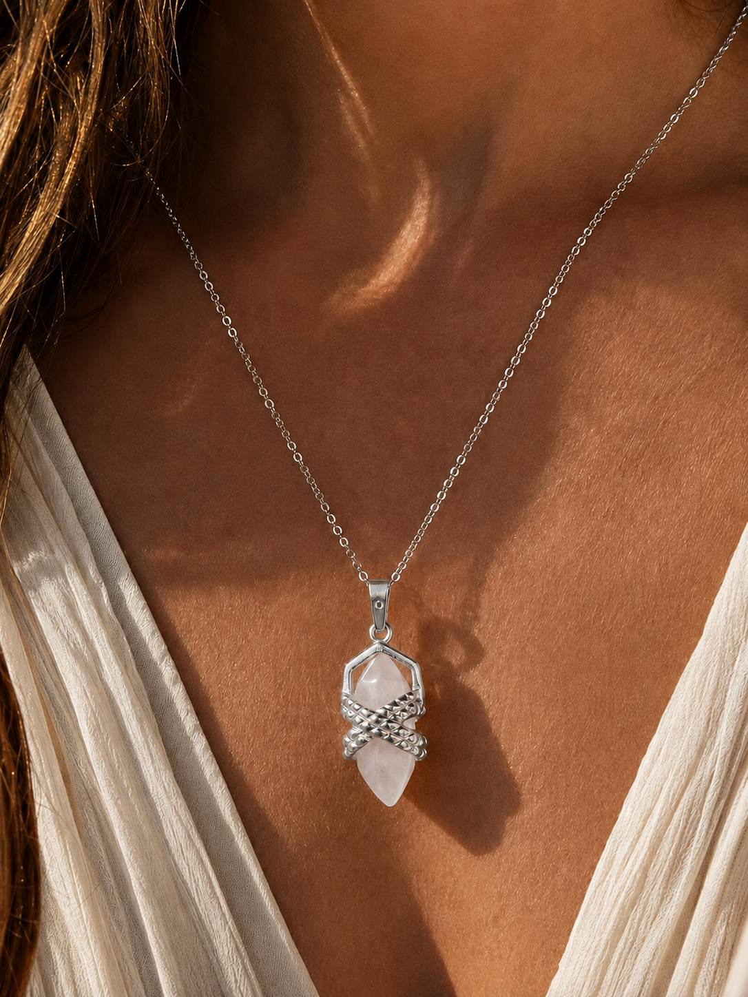 Close-up of a woman wearing a silver quartz crystal pendant necklace on a fine chain in warm natural sunlight.