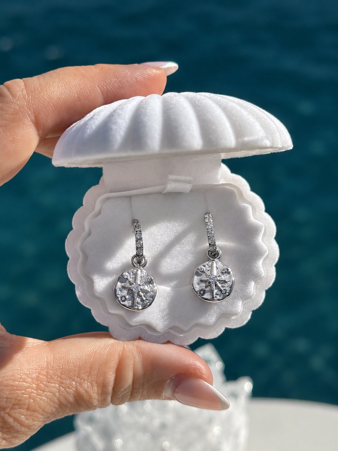Sparkle Star Earrings in silver displayed in a white shell jewellery box against an ocean backdrop. Waterproof celestial huggie earrings with sparkling zircon star charms by Ocean The Label.