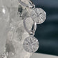 Sterling silver drop earrings with circular starburst charms and pavé-set stones, displayed on a clear crystal cluster against a dark blue background.