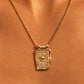 A gold chain necklace with a rectangular pendant featuring a sun and wave design, shown worn on a model's neck against a warm skin-toned background.