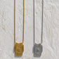 Pendant sun necklaces hanging from chains on a textured white stone surface. One necklace is gold-toned with a gold pendant, and the other is silver-toned with a silver pendant.