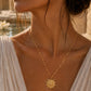 Delicate gold chain necklace with a circular sunburst pendant, set against a warm, sunlit outdoor background.