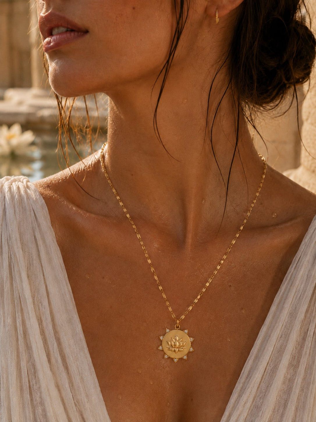 Delicate gold chain necklace with a circular sunburst pendant, set against a warm, sunlit outdoor background.