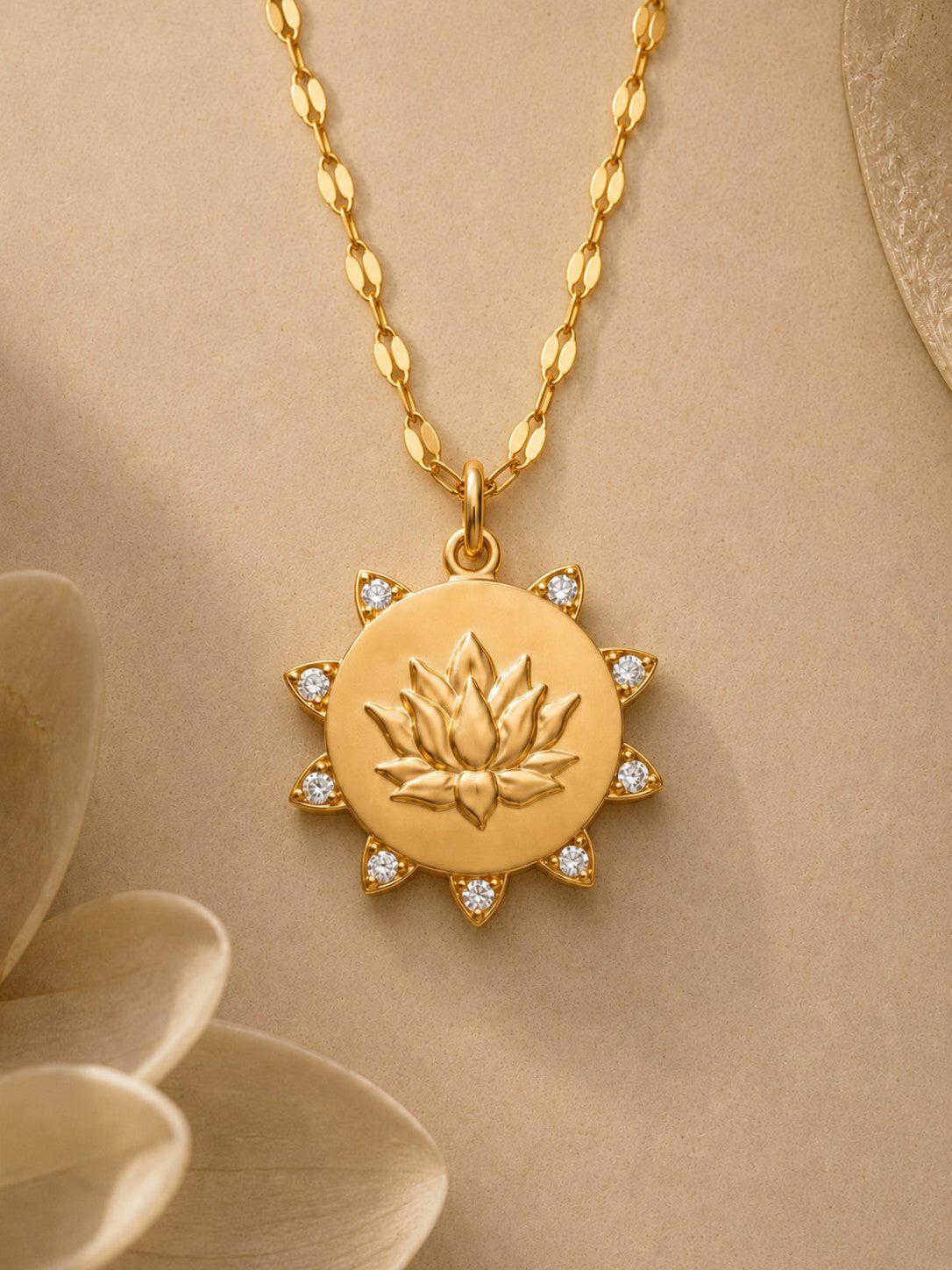 A gold pendant necklace featuring a lotus flower design in the center, surrounded by small clear stones, hanging from a gold chain against a warm beige background with soft decorative petals.