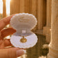 A hand holds an open white clamshell jewelry box with the brand name 'Ocean The Label' printed inside. The box contains a gold pendant necklace.