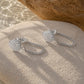 A pair of silver shell-shaped drop earrings with short chain links, displayed on a textured beige stone with a larger rock in the background.