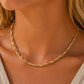 A close-up of a woman's neck and chest wearing a delicate twisted gold chain necklace.