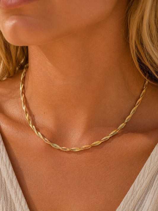 A close-up of a woman's neck and chest wearing a delicate twisted gold chain necklace.