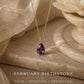 A gold pendant necklace with a teardrop-shaped purple gemstone is displayed on a beige stone surface next to a white flower. Text at the bottom reads 'FEBRUARY BIRTHSTONE' with additional descriptive words.