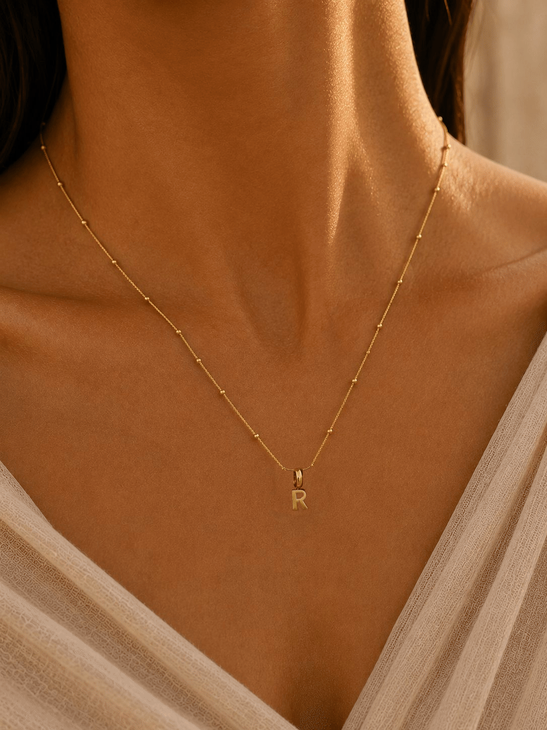 Model wearing a gold Letter Charm Necklace as J, R and N initial charms are added one by one.