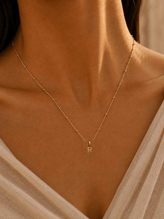 Model wearing a gold Letter Charm Necklace as J, R and N initial charms are added one by one.