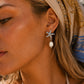 A close-up of a woman wearing a silver starfish dangle earring with a white pearl drop, styled with a patterned beige and blue headscarf.