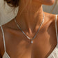 A close-up lifestyle shot of a woman wearing a silver snake chain necklace with a small clear crystal pendant, styled with a white spaghetti strap top under warm sunlight.